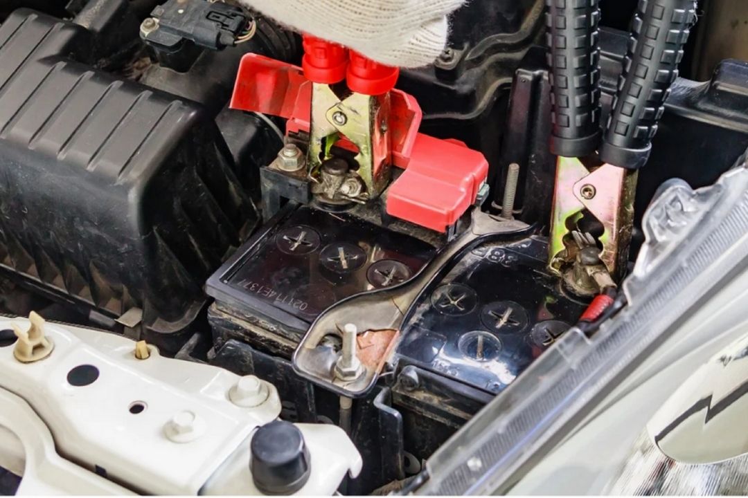 Close-up of a car battery with jumper cables attached to the terminals and a wrench placed on top, indicating maintenance or jump-starting in progress.