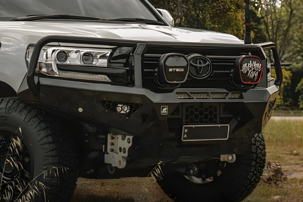 Close-up of the front of a white Toyota SUV with an off-road bumper, large tires, auxiliary lights, and a red "Let's Explore" cover on one light—ready for outdoor adventures and mechanical maintenance and repair in any terrain.