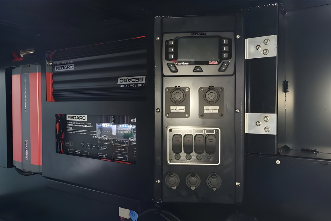 REDARC power management panel with monitor, power outlets, toggle switches, and charging ports—ideal for diesel mechanical services—mounted alongside a REDARC inverter and battery management system in a dark enclosure.